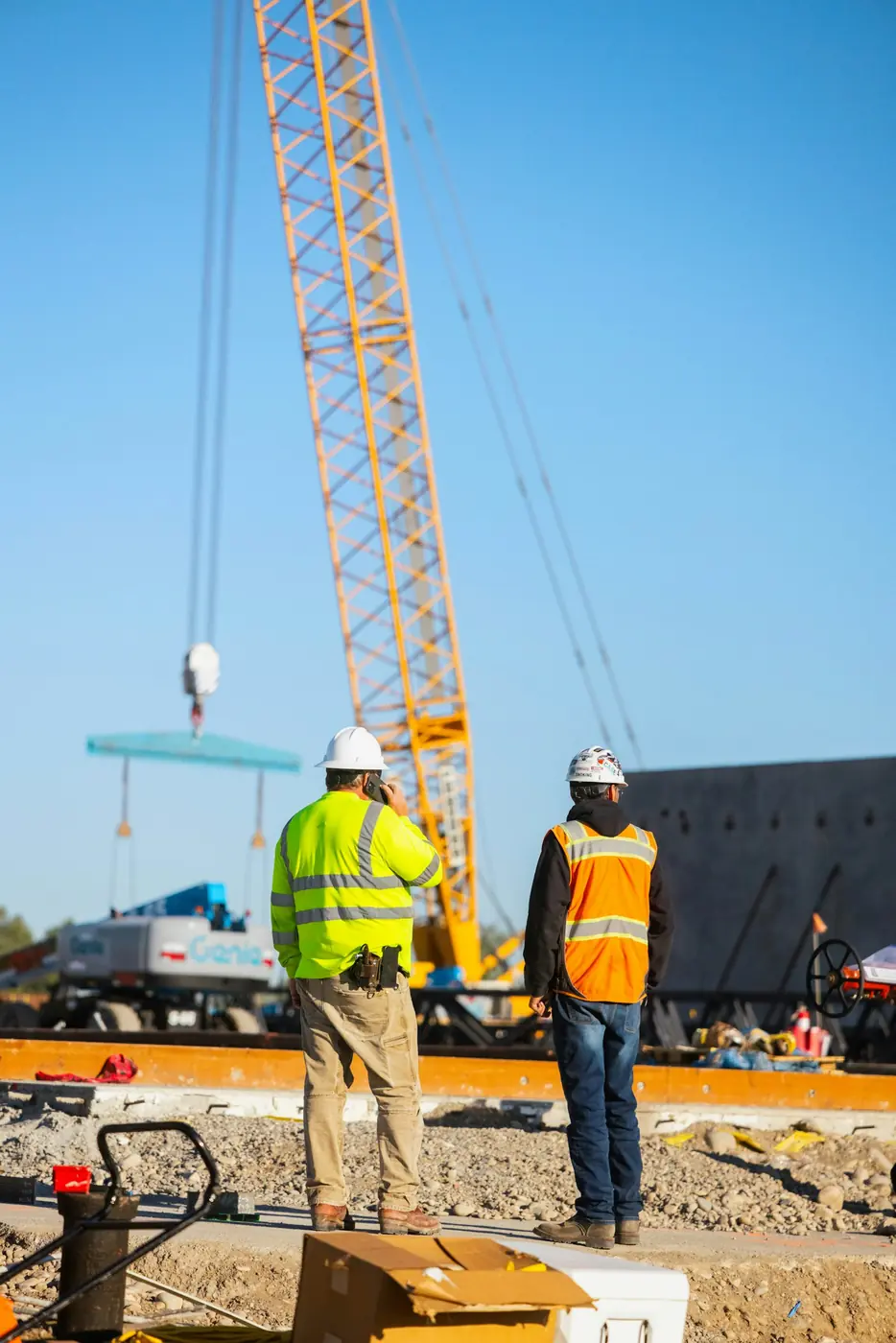 Two crew members in hard hats watching a crane lift on a job site