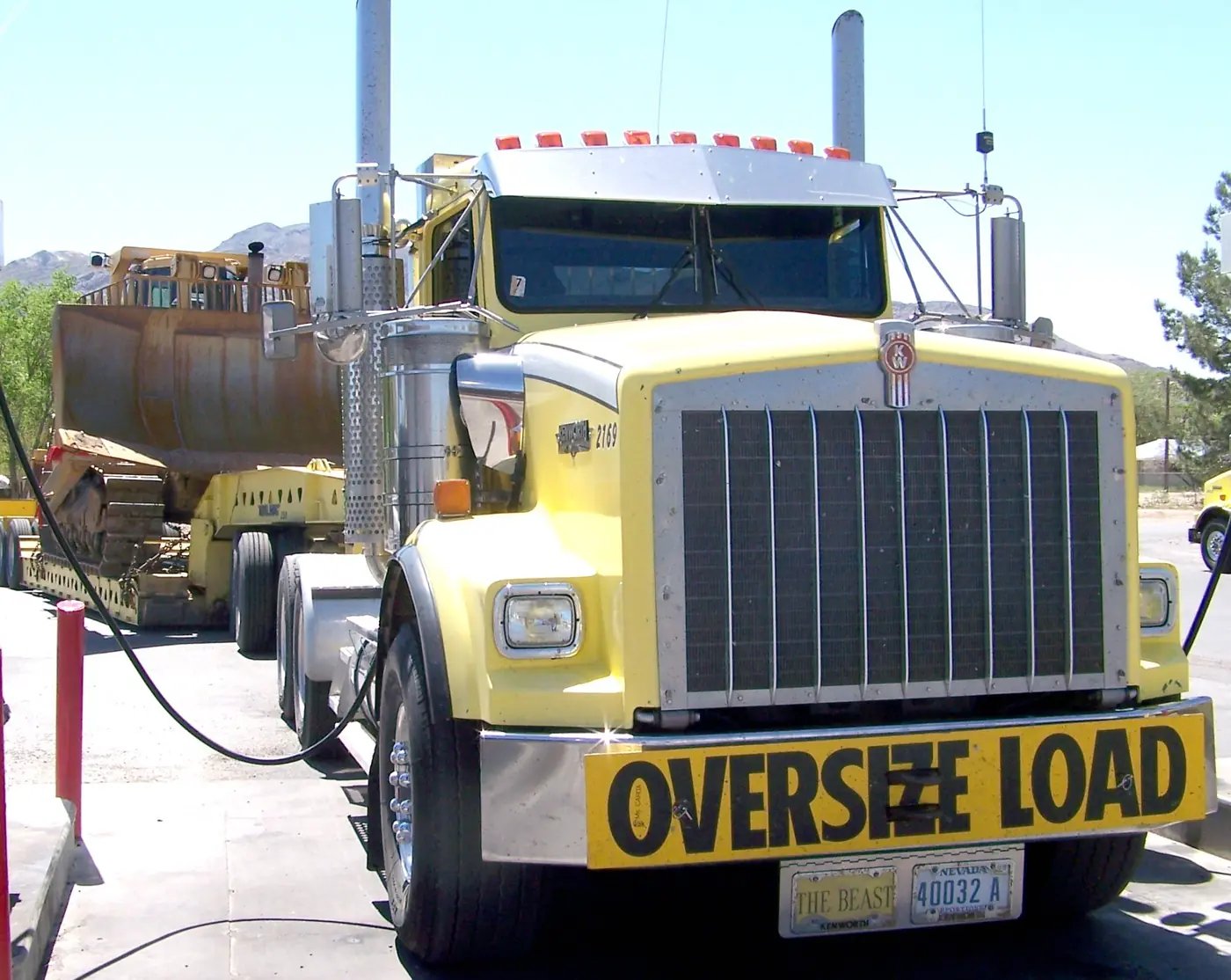 A Kenworth T800 with an oversize-load banner hauling a Caterpillar D9R bulldozer on a lowboy trailer