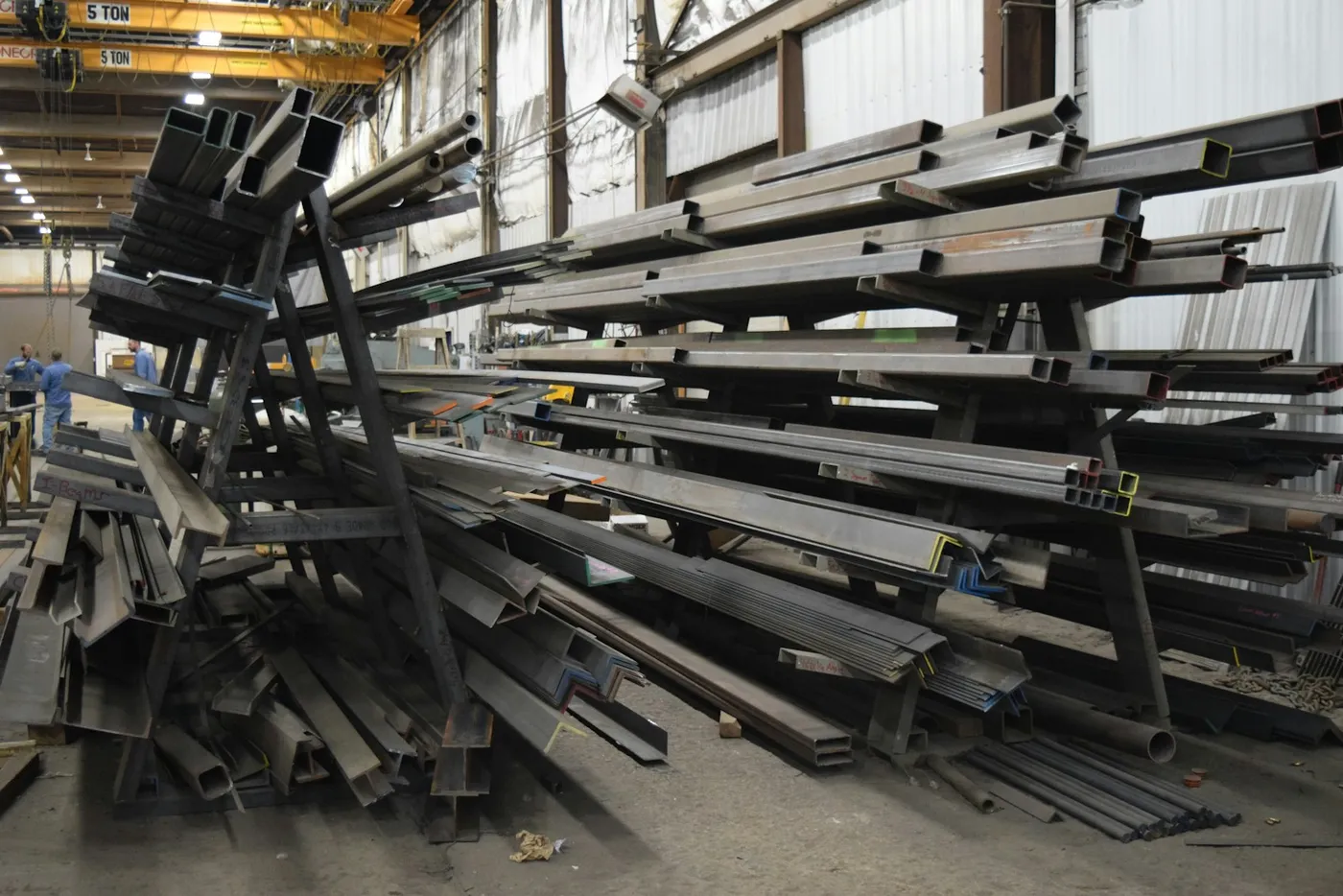 Racks of steel beams and tubing in a supplier’s warehouse under a 5-ton overhead crane