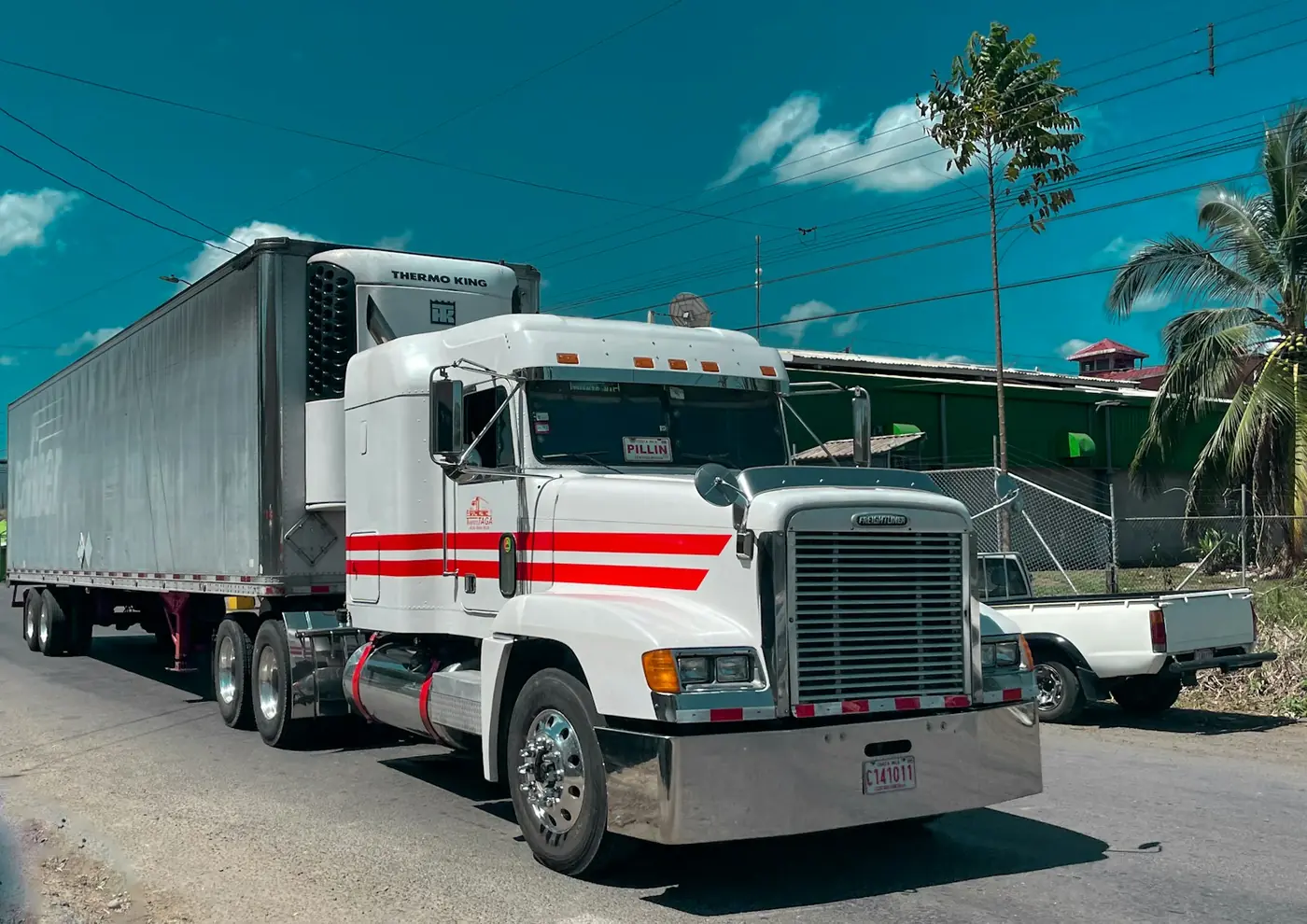 A white Freightliner semi truck with a refrigerated trailer