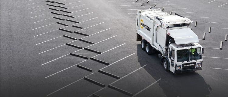 A white Mack garbage truck navigating through an empty parking lot